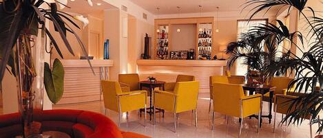 A modern hotel lobby with a bar area, yellow chairs, and large potted plants.