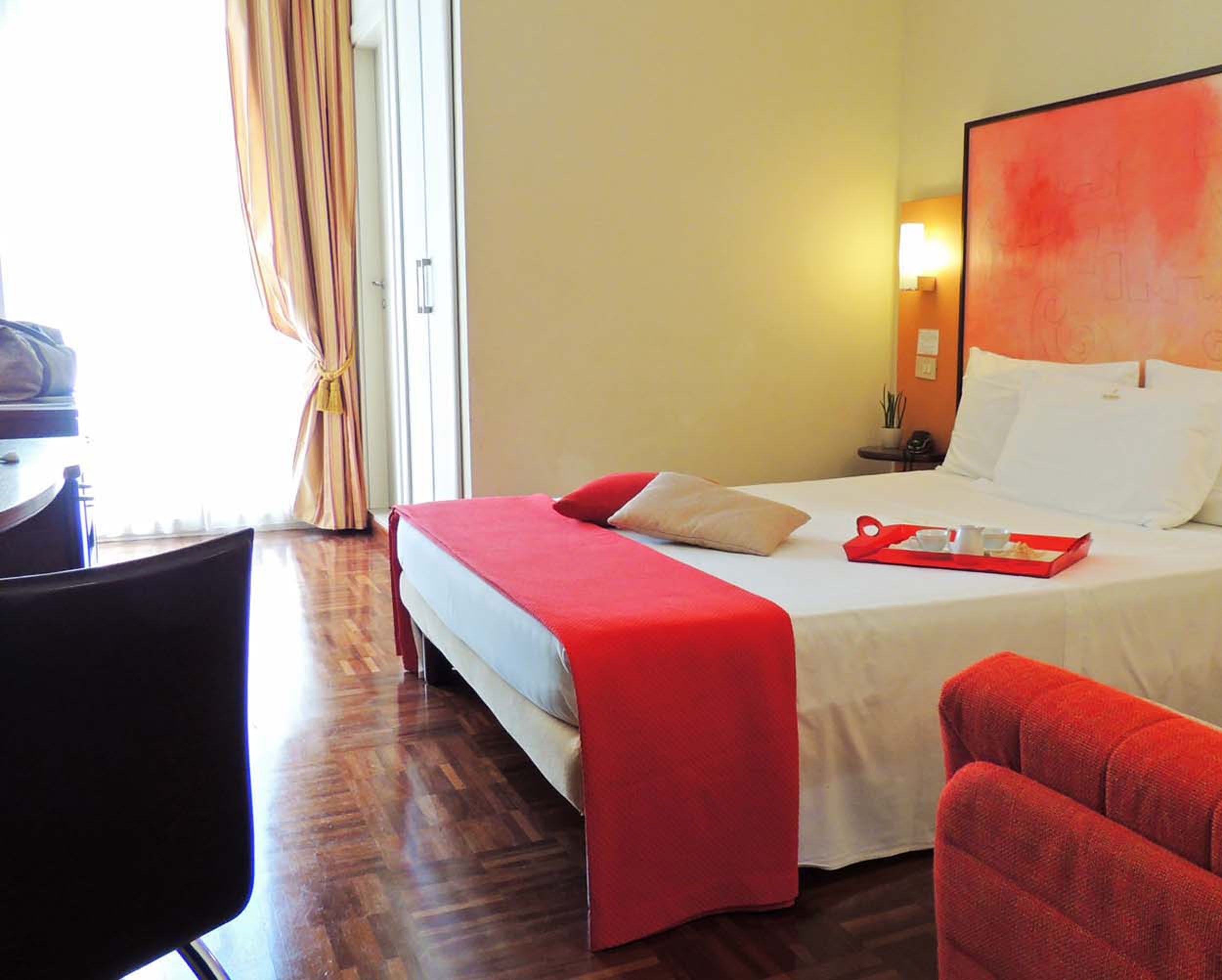A hotel room with a bed, a chair, a table, and a window with curtains.