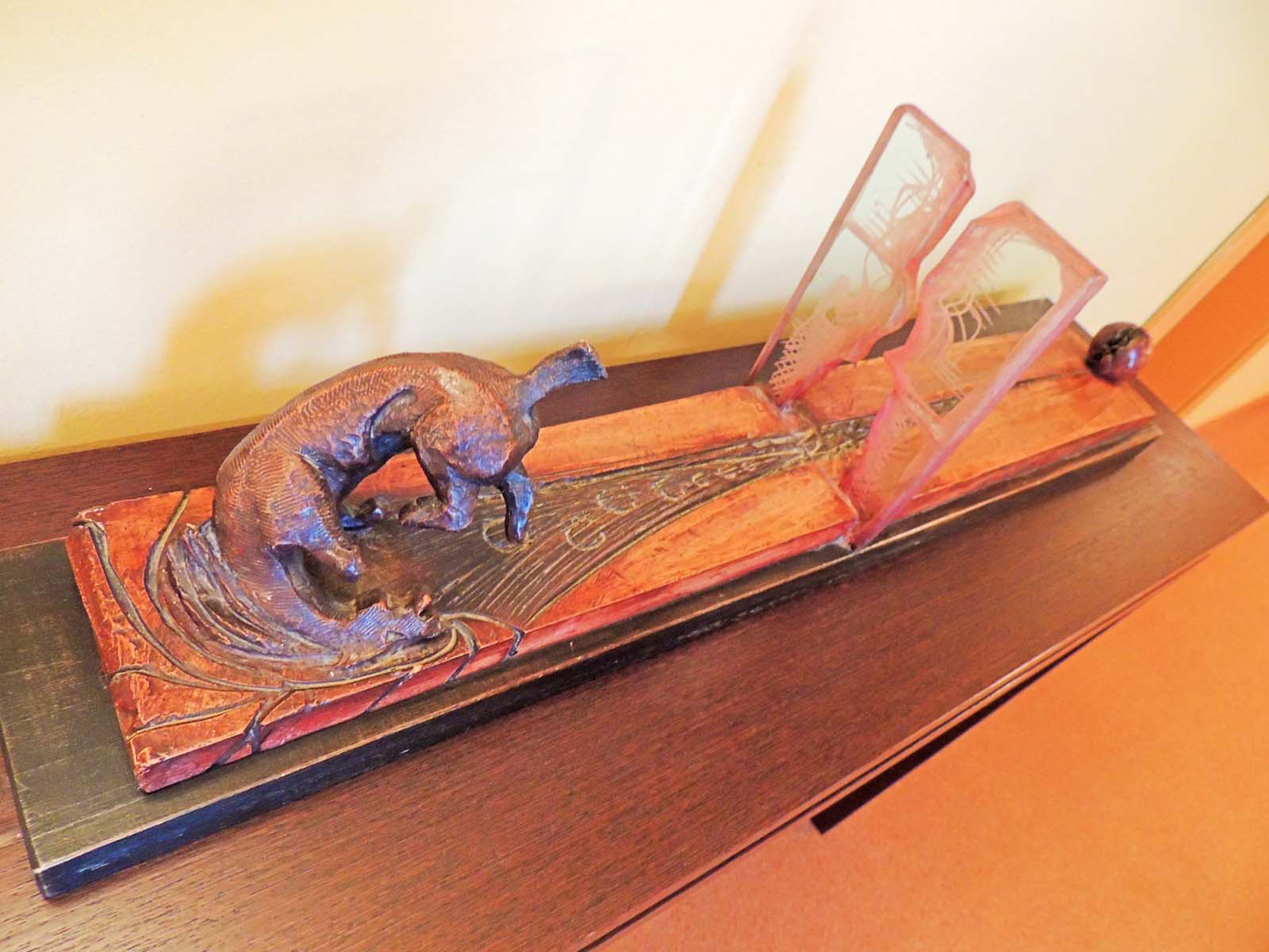 Een houten tafel met een uitgesneden dinosaurusbeeldje en een doorzichtig plastic voorwerp.
