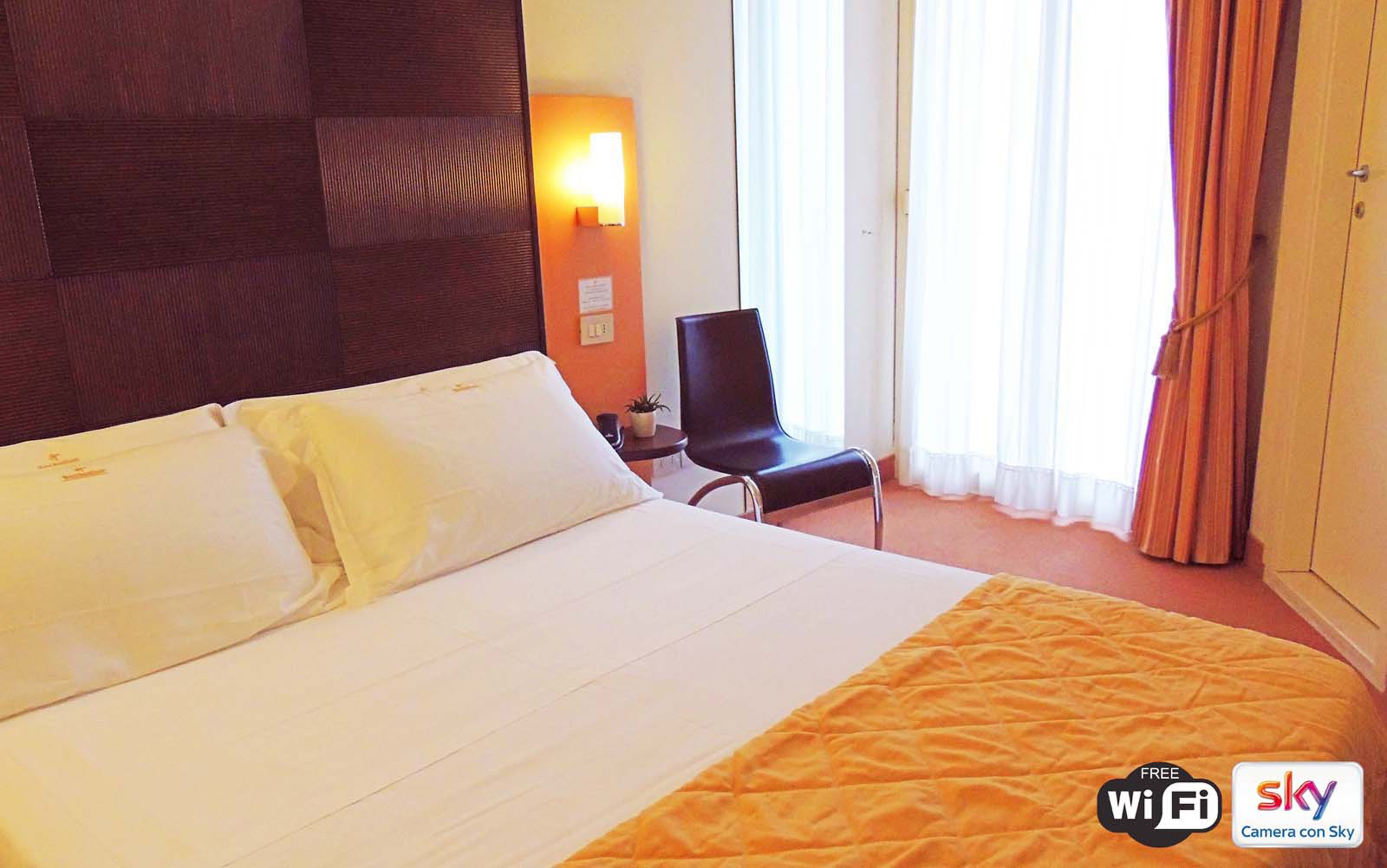 A hotel room with a large bed, a chair, a desk, and a window with curtains.