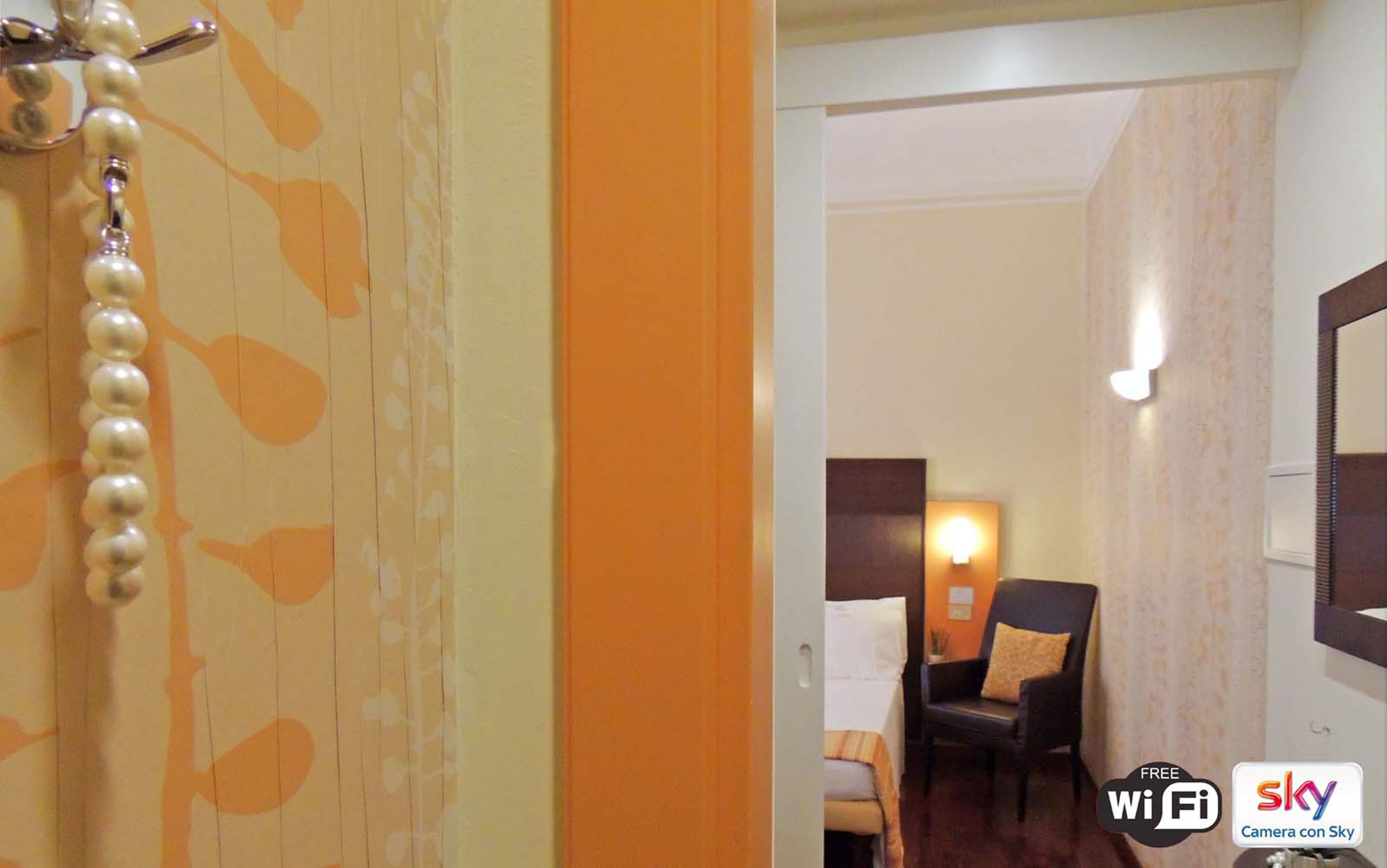 Una habitación de hotel con una cama, una silla, una mesita de noche y una lámpara de pared.