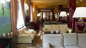 A spacious lobby with multiple seating areas, including sofas and armchairs, a marble floor, and a large window with curtains.