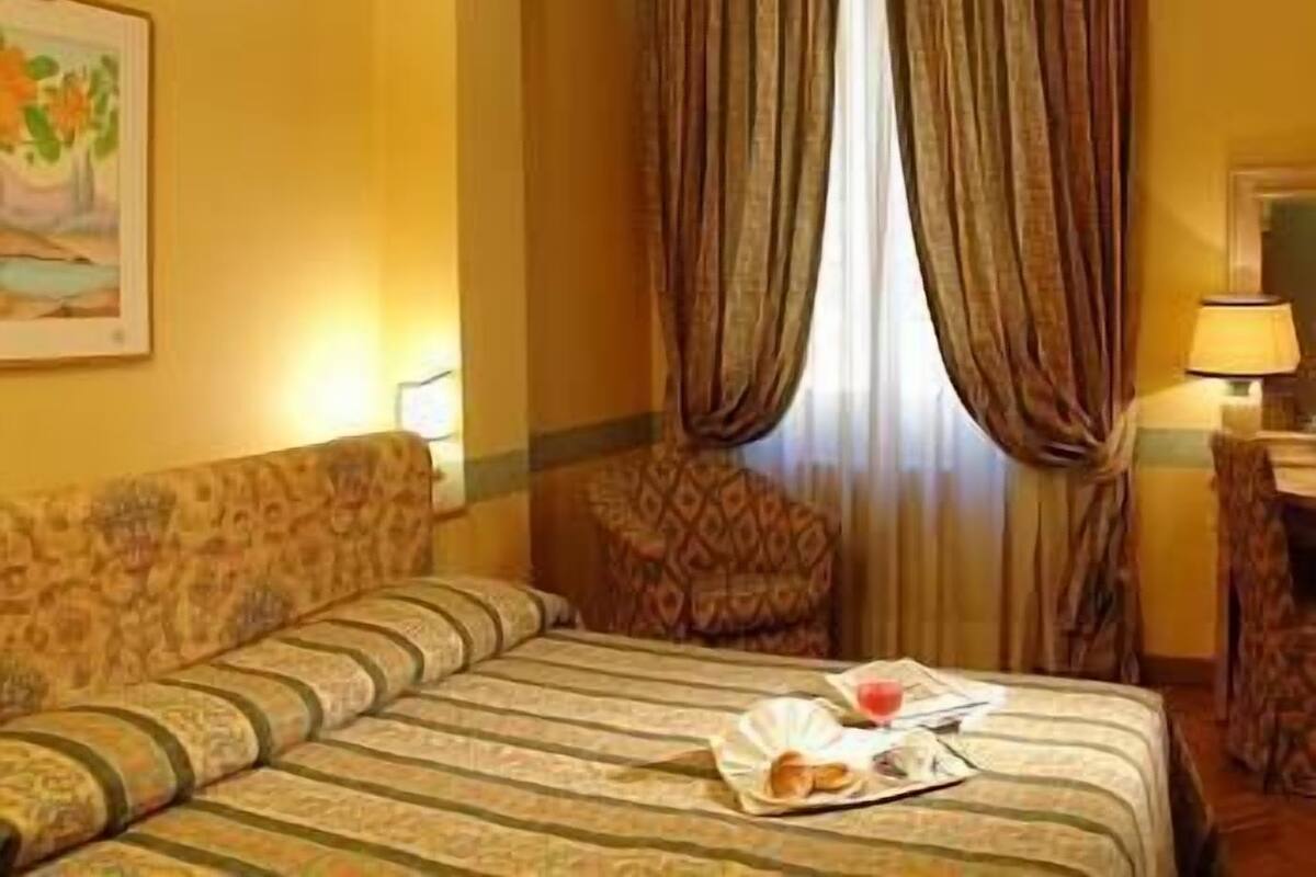 A hotel room with a bed, a chair, a table with a lamp, and a painting on the wall.