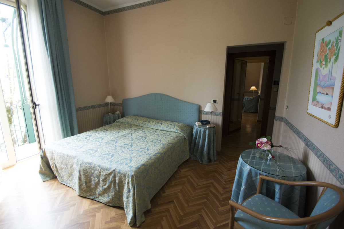 A bedroom with a bed, bedside tables, a chair, and a small table with a vase of flowers.