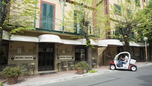 A building with a sign reading "HOTEL GIGLIO" and outdoor seating with umbrellas.