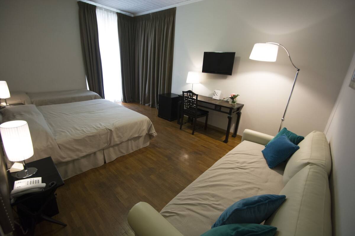 A hotel room with two beds, a desk, a chair, a TV, and a lamp.