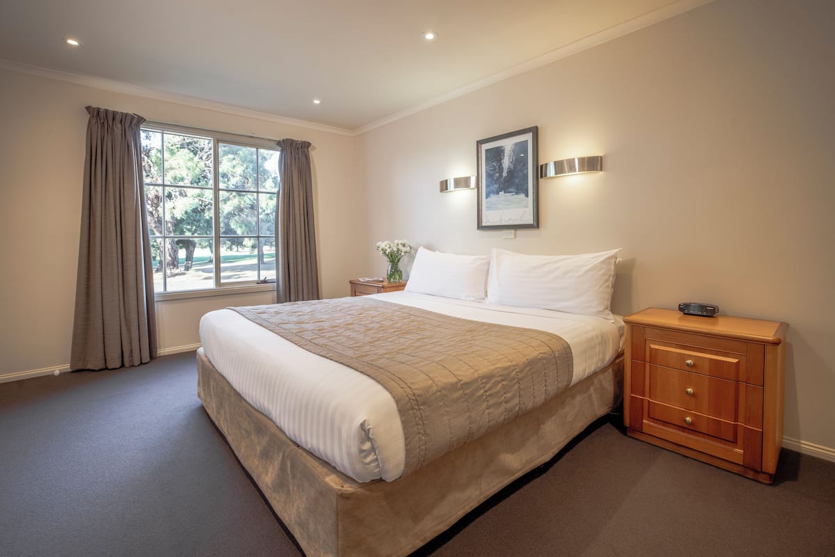 Une chambre à coucher avec un grand lit, une table de chevet, une commode et une fenêtre avec des rideaux.