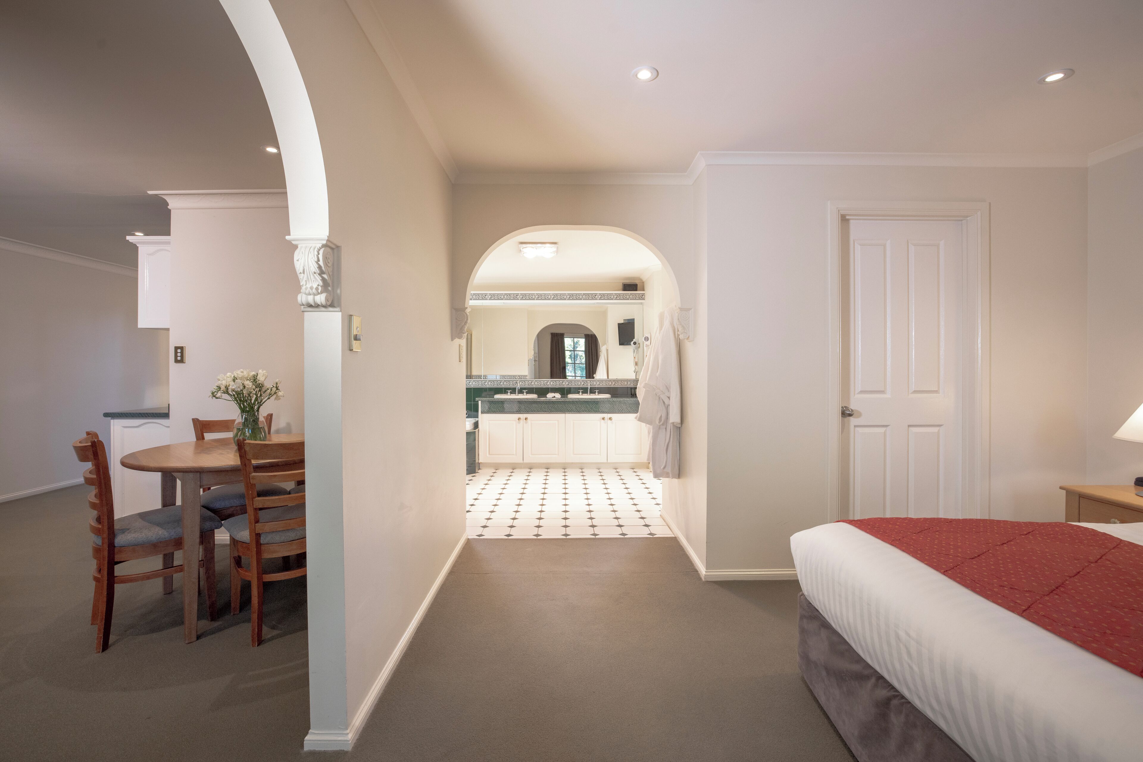 A hotel room with a bed, a dining table with chairs, a kitchen area, and a bathroom.