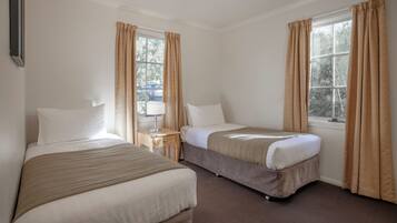 A hotel room with two beds, a nightstand, a lamp, and a window with curtains.