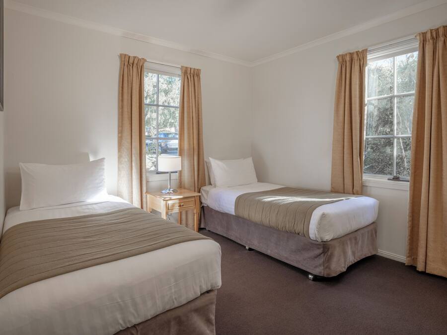 A hotel room with two beds, a nightstand, a lamp, and a window with curtains.
