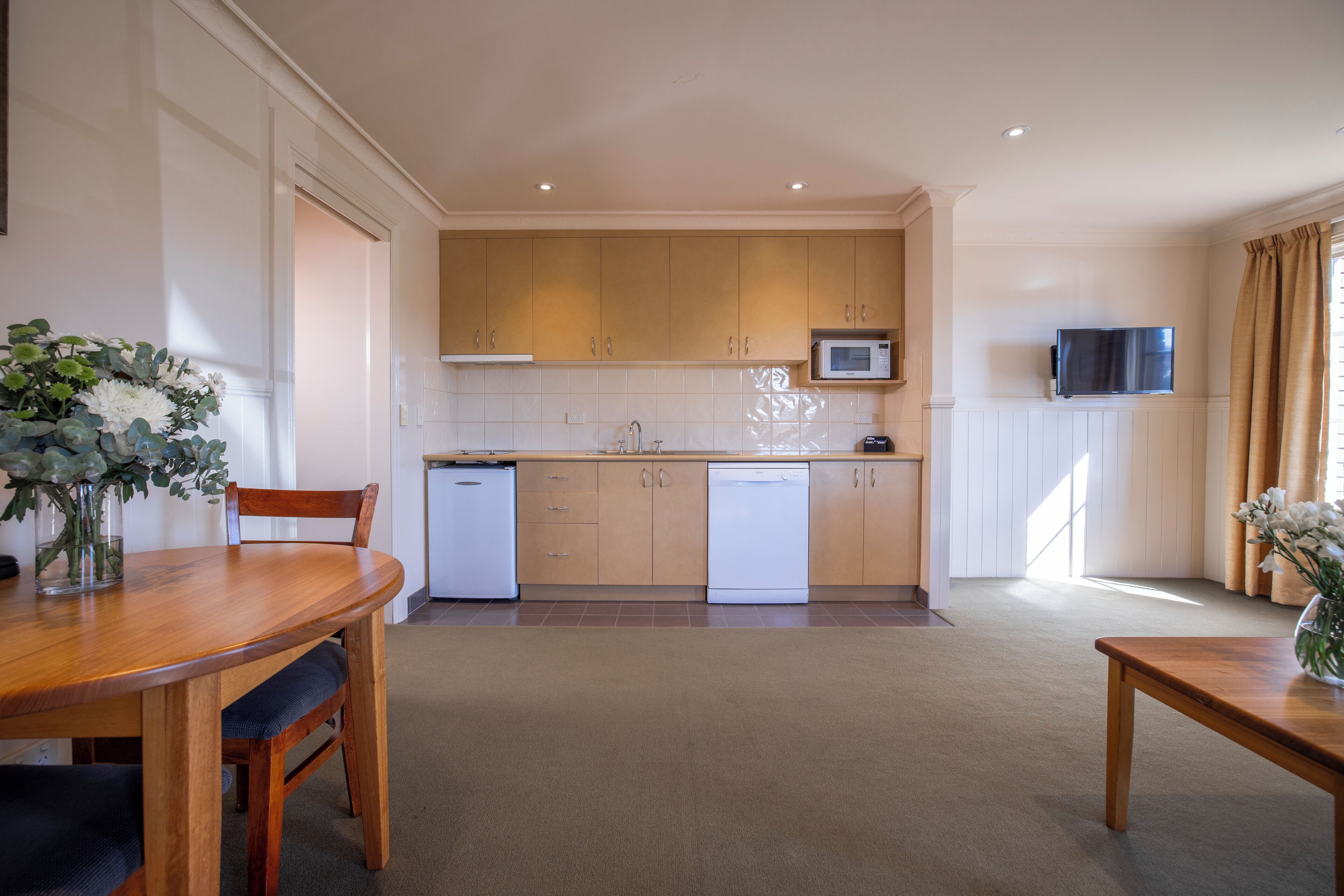 A modern kitchen with wooden cabinets, a microwave, and a dishwasher. There is a dining table with chairs and a vase with flowers on it.