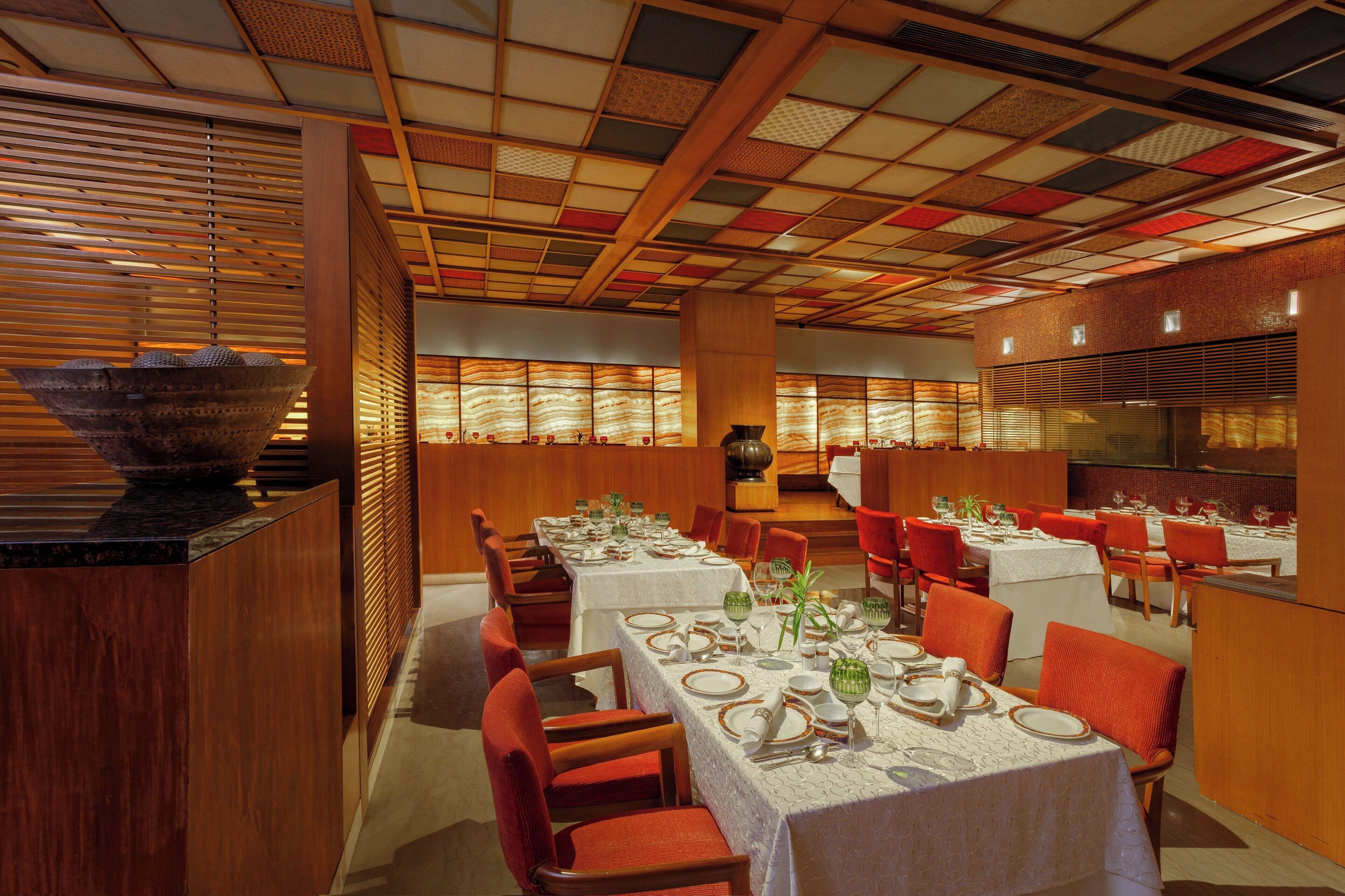 A restaurant with multiple tables set for dining, wooden paneling, and a patterned ceiling.
