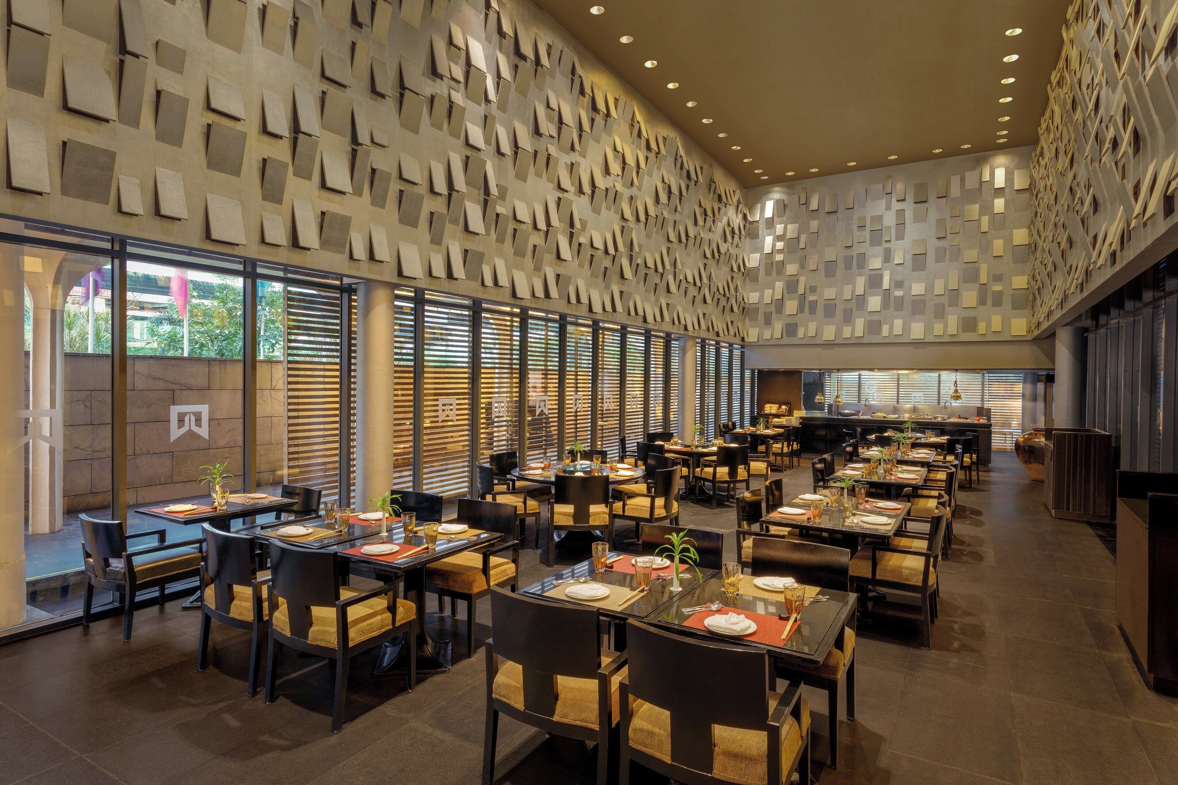 A spacious restaurant with multiple dining tables and chairs, a patterned ceiling, and large windows allowing natural light.