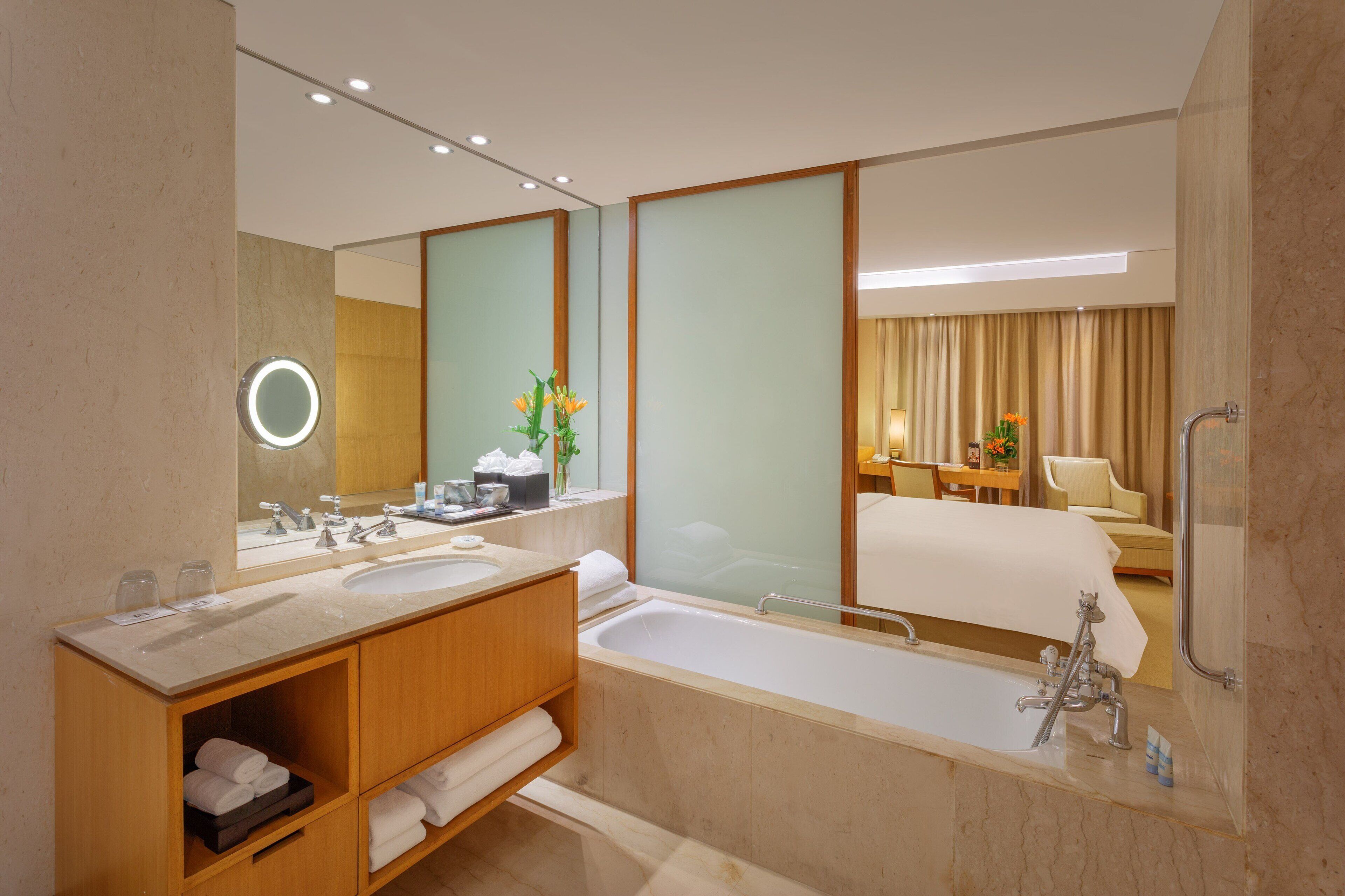 Une salle de bain d’hôtel moderne, dotée d’une grande baignoire, de deux lavabos, d’une coiffeuse avec miroir et d’un espace douche.