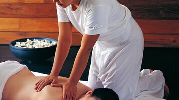 A person receiving a back massage in a room with wooden walls and a bowl of flowers on a table.
