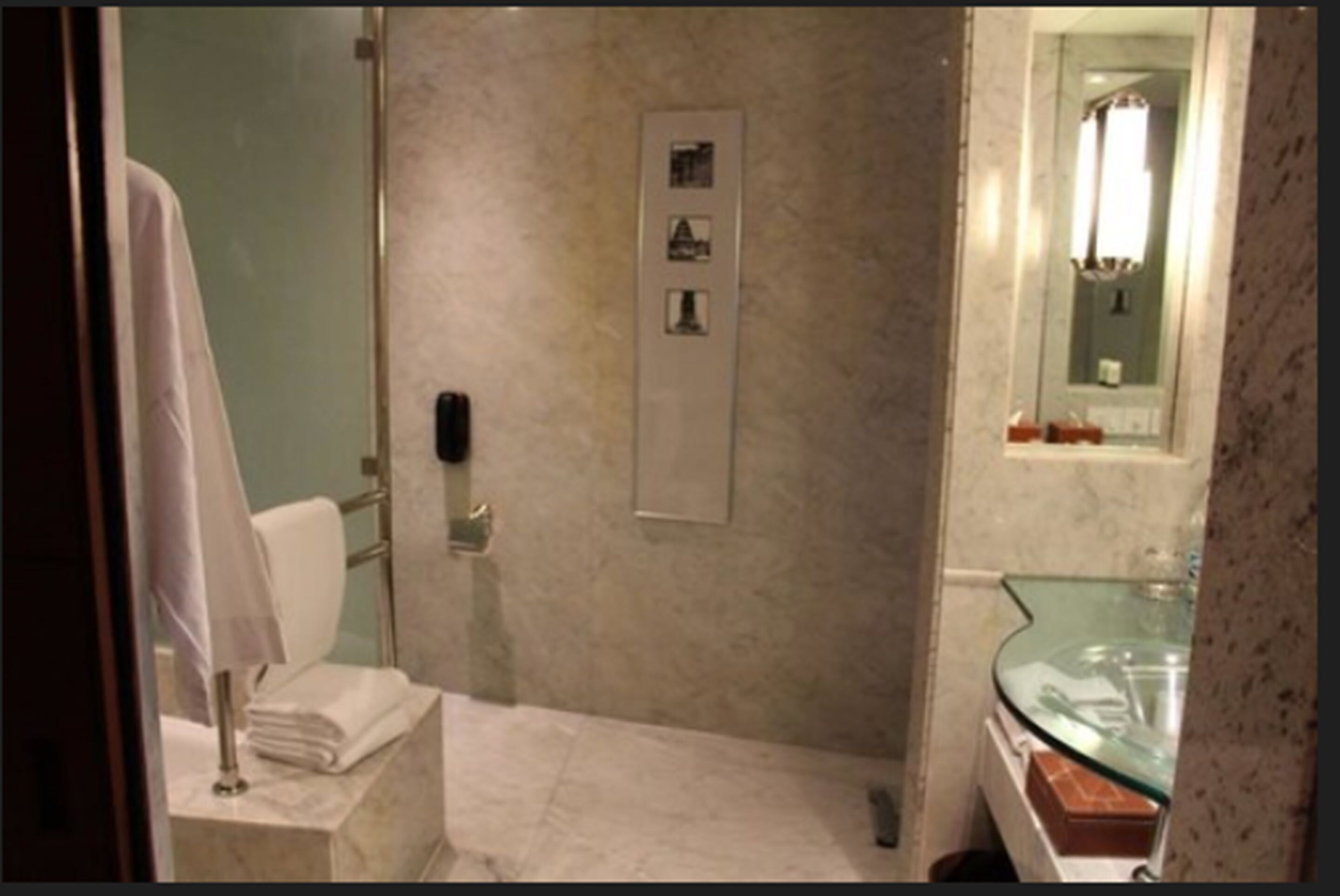 A bathroom with a glass shower enclosure, a marble wall, and a glass sink.