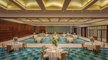 A large banquet hall with multiple round tables set for dining, featuring a checkered floor pattern and recessed lighting on the ceiling.