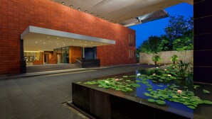 A modern building with a brick facade, a large entrance, and a water feature with lily pads and flowers.