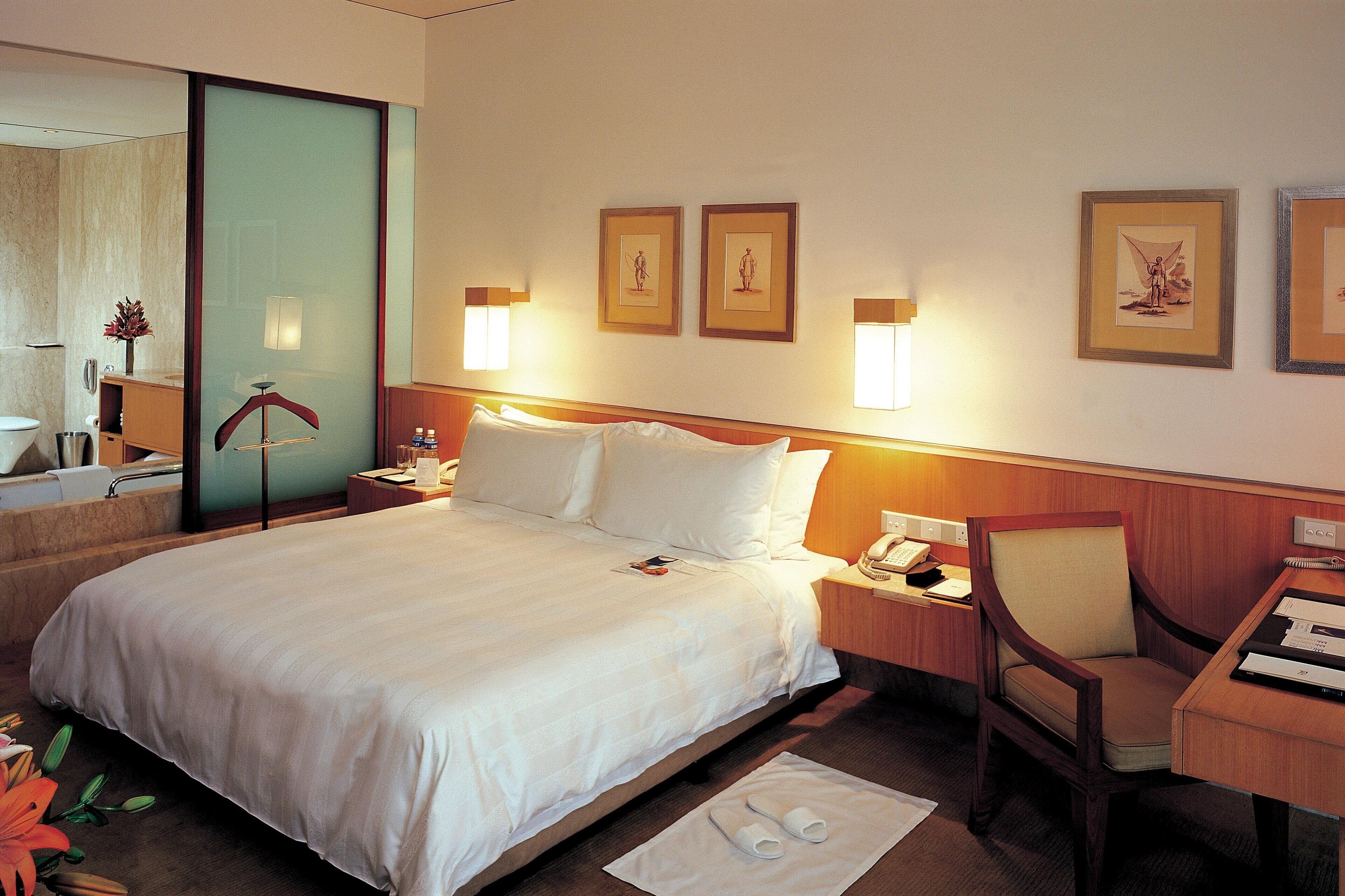 A hotel room with a large bed, a desk, a chair, and a nightstand. There are framed pictures on the wall and a vase with flowers on the desk.