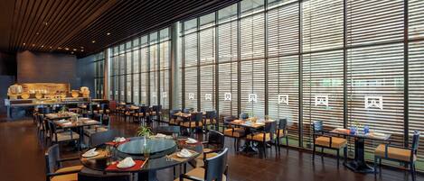 Un restaurante espacioso con techos altos y grandes ventanales, que cuenta con varias mesas y sillas para comer.