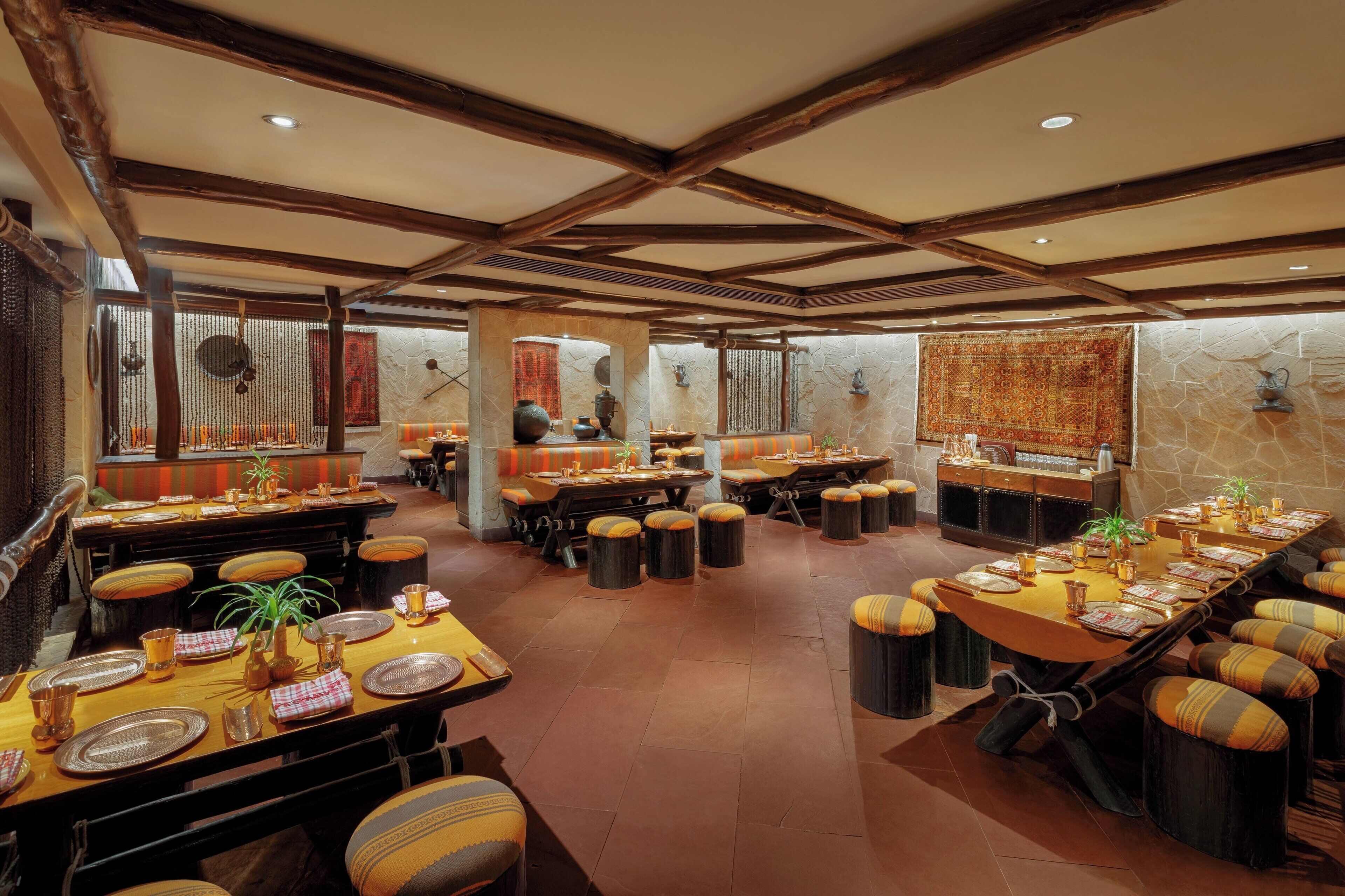 A spacious restaurant with multiple dining tables and booths, featuring a rustic wooden ceiling and stone walls.