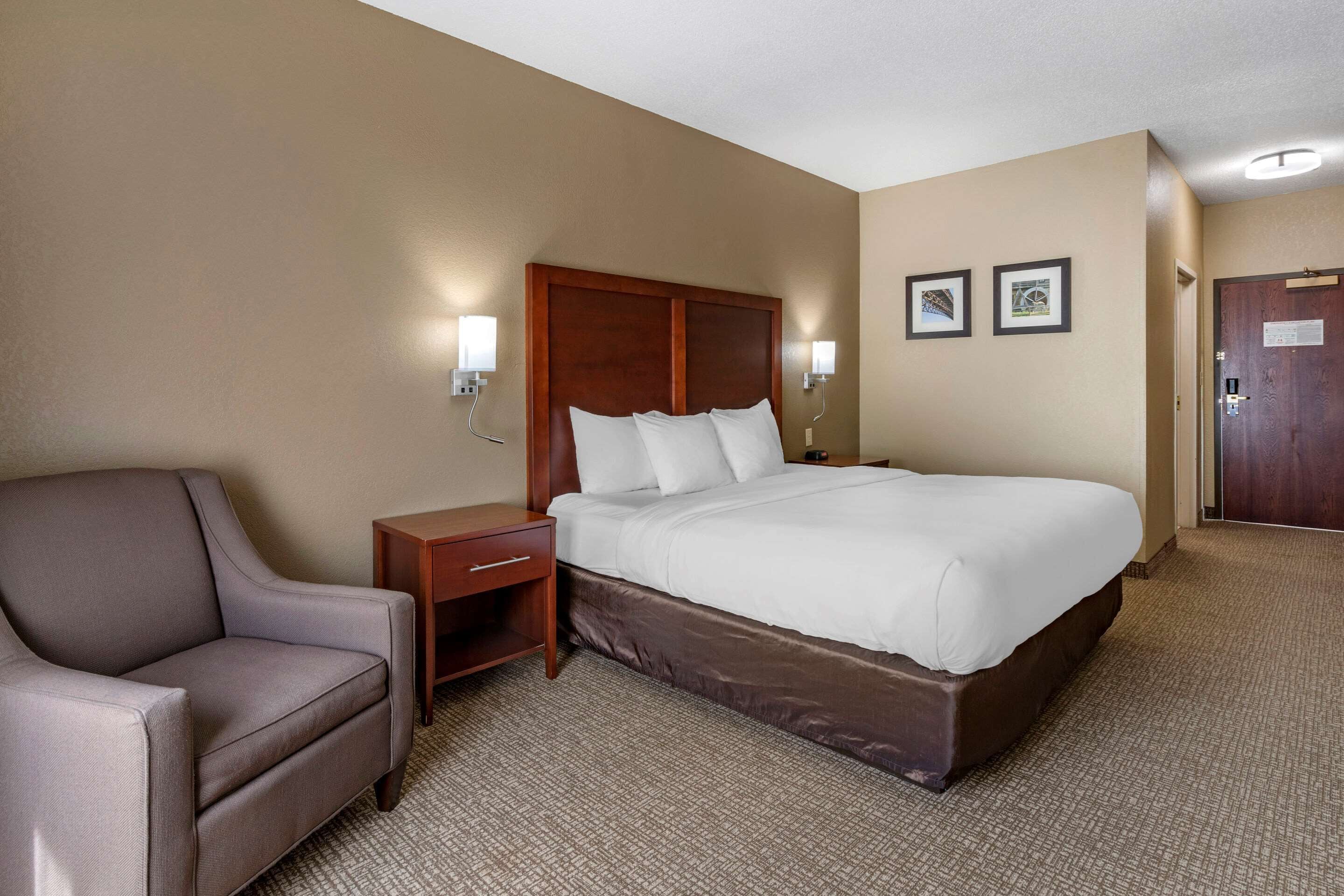 Habitación de hotel con una cama grande, una mesita de noche, una silla y dos lámparas fijadas a la pared.
