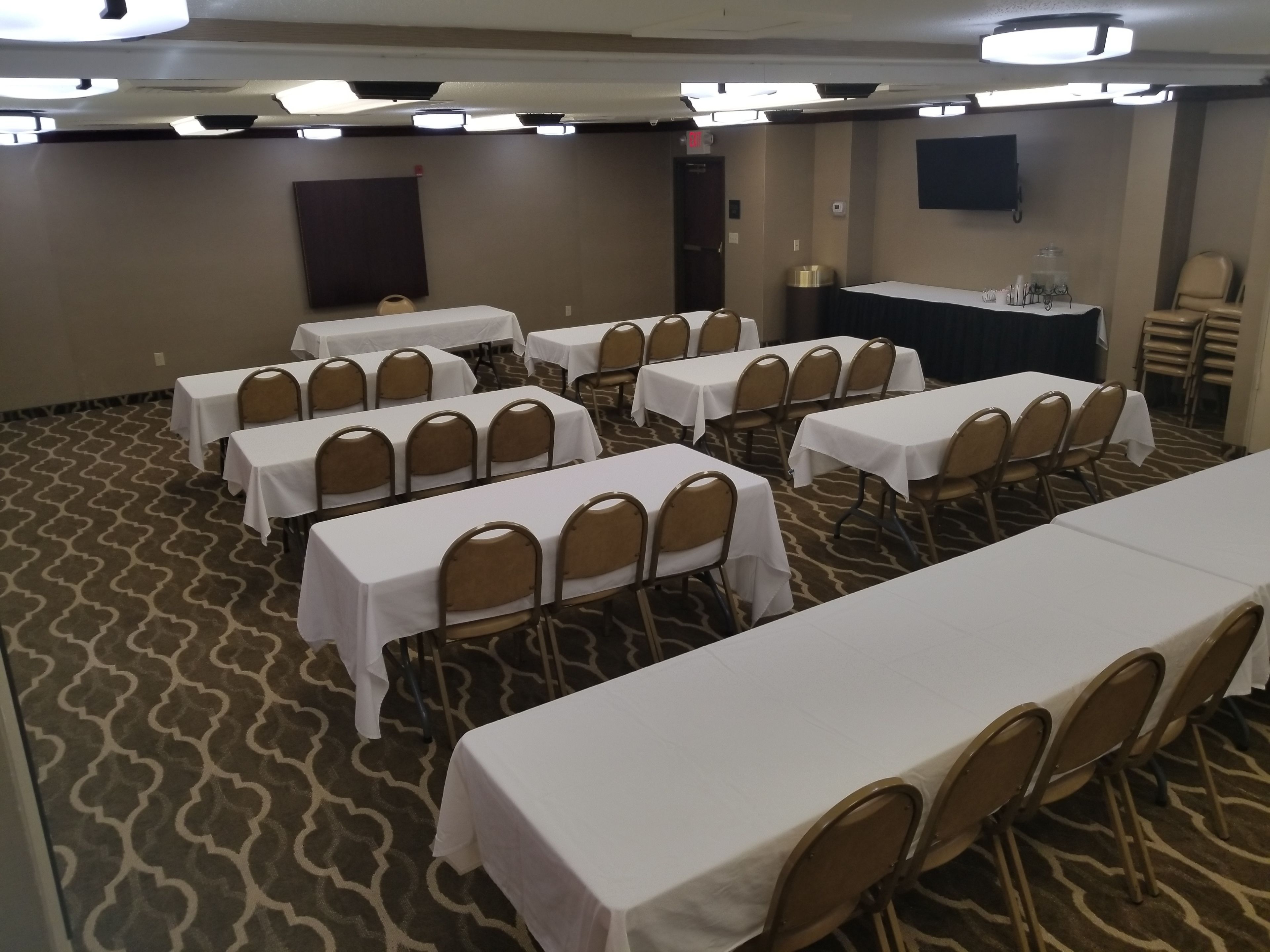 A conference room with multiple tables and chairs, carpeted floor, and ceiling lights.
