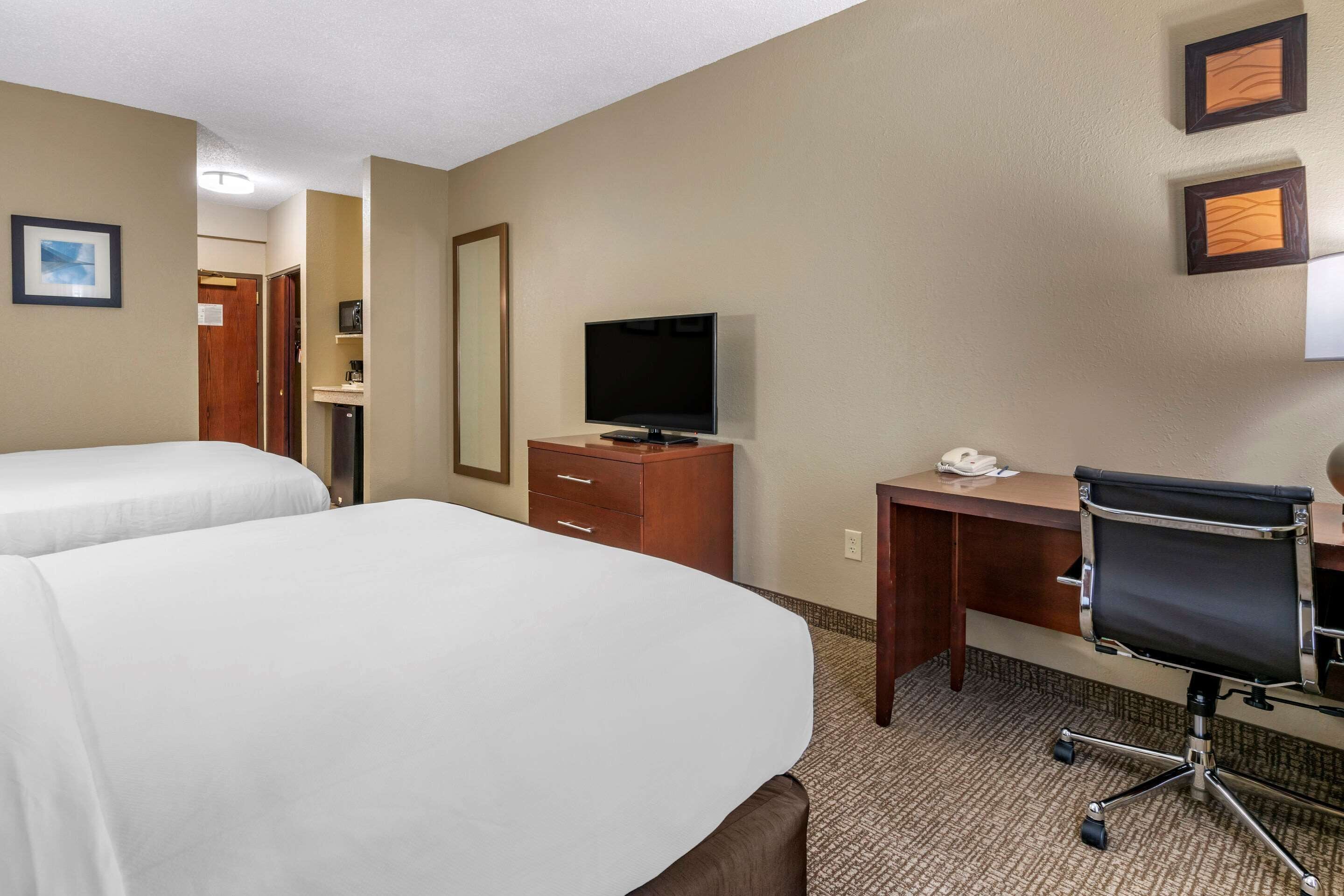 A hotel room with two beds, a desk, a chair, a television, and a mirror.