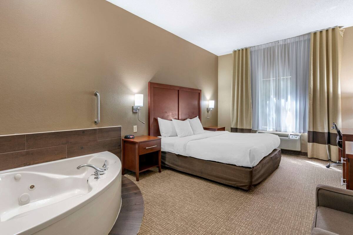 A hotel room with a large bed, a separate bathroom with a bathtub, and a desk with a chair.