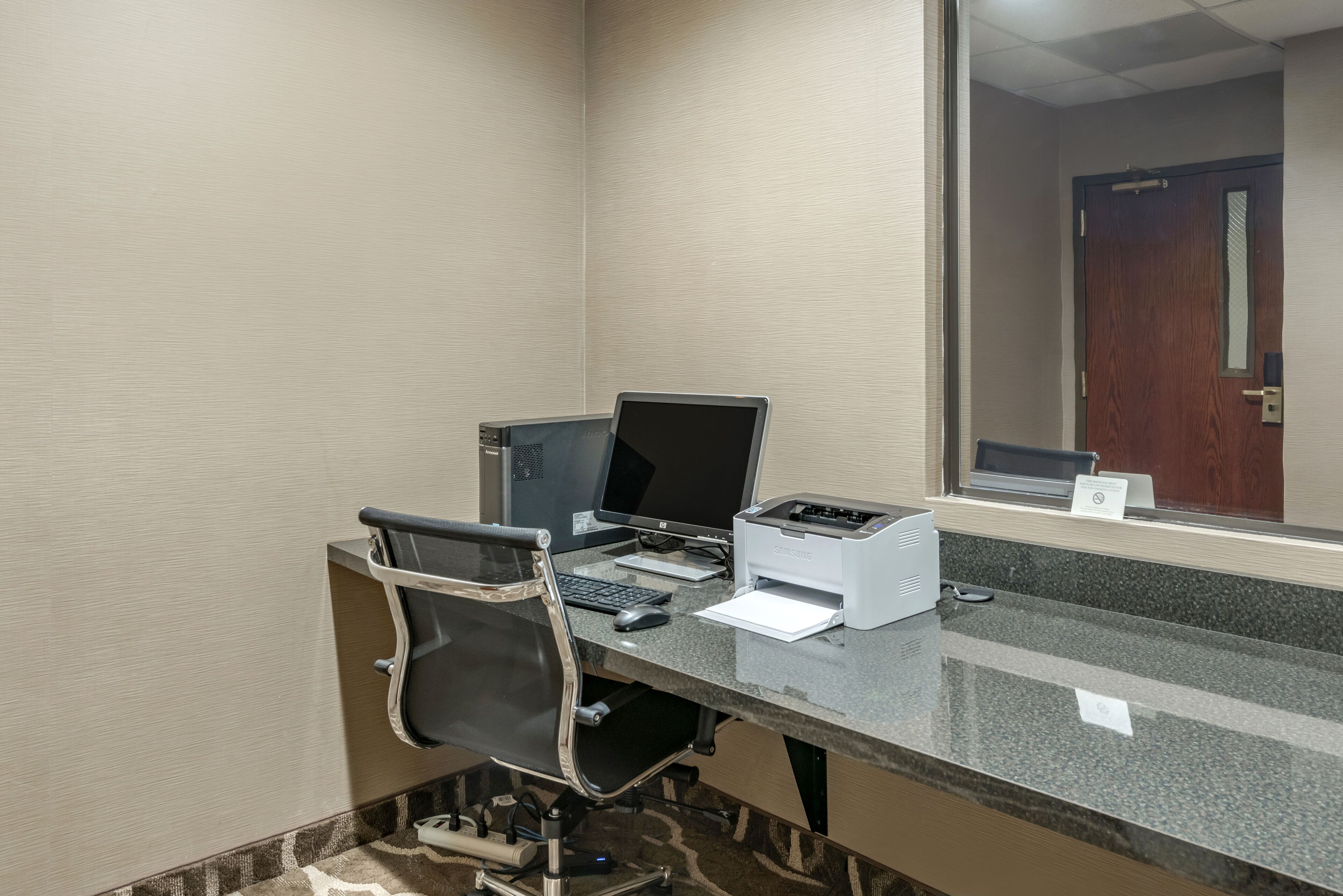 A hotel room with a desk, two monitors, a printer, and a chair.