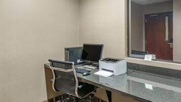 A hotel room with a desk, two monitors, a printer, and a chair.