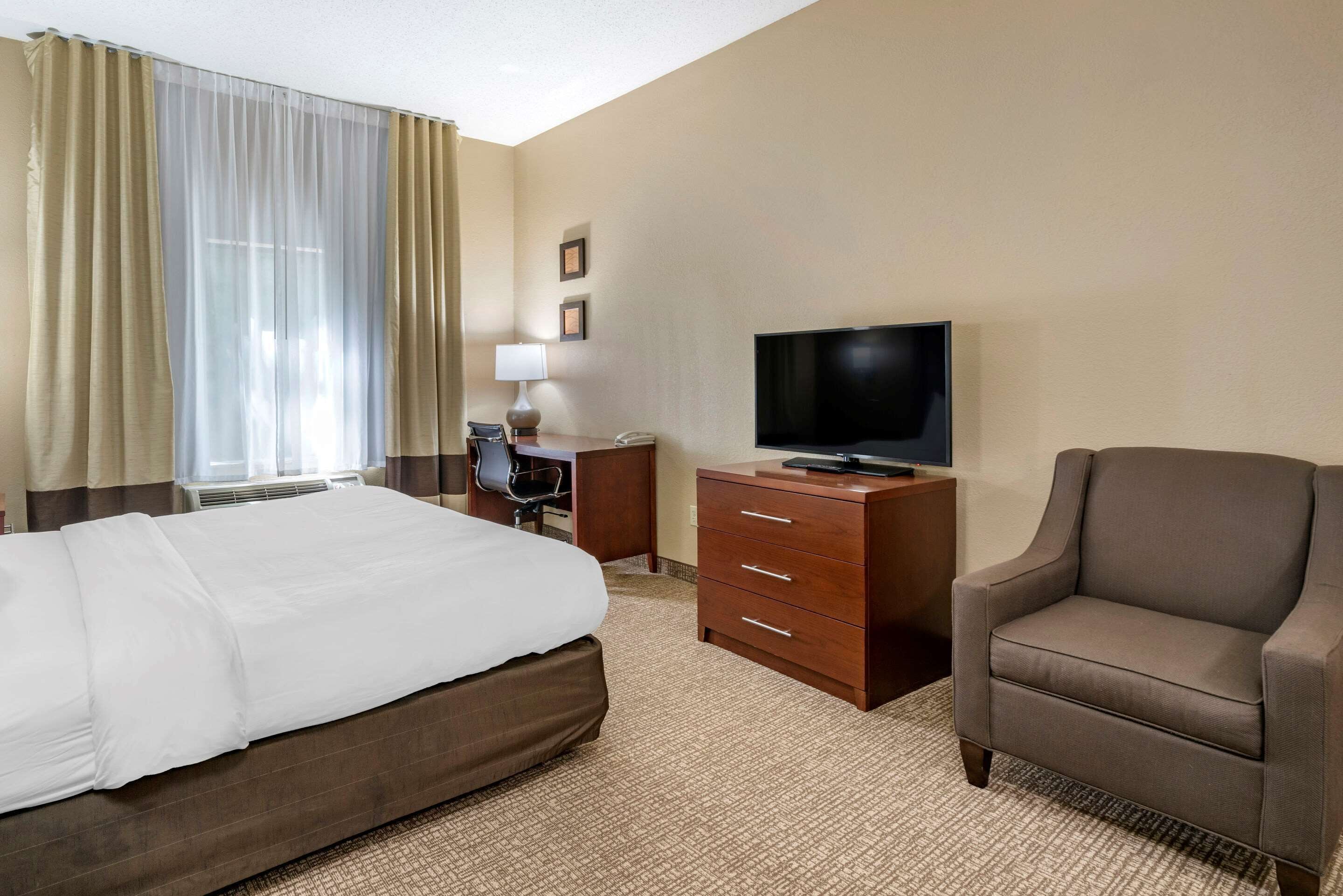 A hotel room with a bed, a desk, a chair, a television, and a lamp.