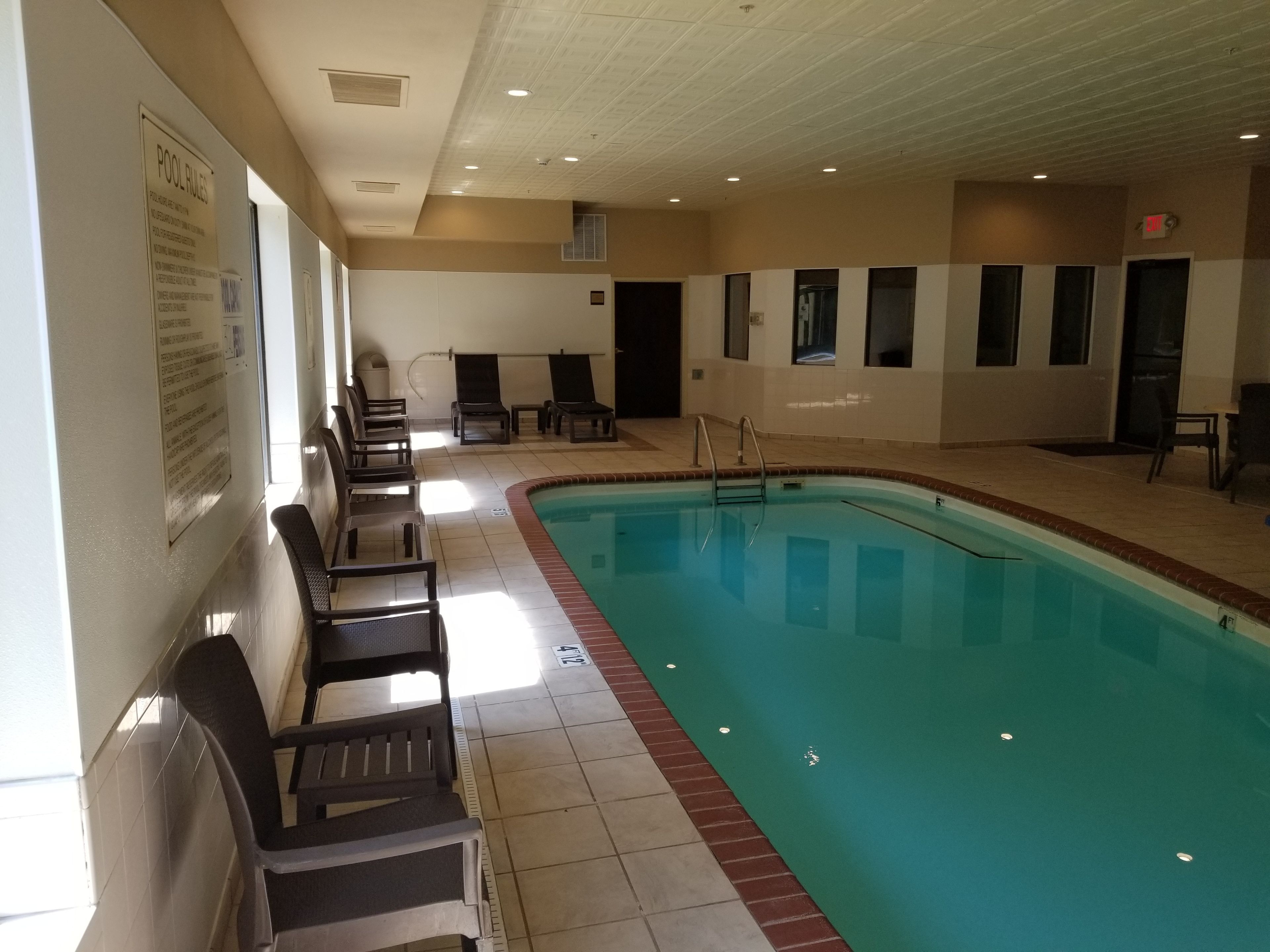 An indoor swimming pool with lounge chairs and a pool rule sign on the wall.