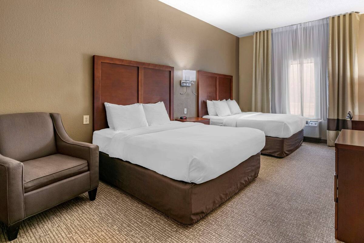 A hotel room with two beds, a sofa, a desk, and a large window with curtains.