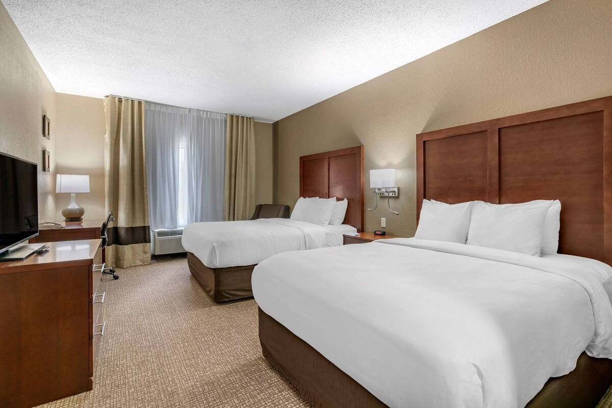 A hotel room with two beds, a desk, a TV, and a window with curtains.