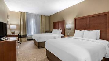 A hotel room with two beds, a desk, a TV, and a window with curtains.