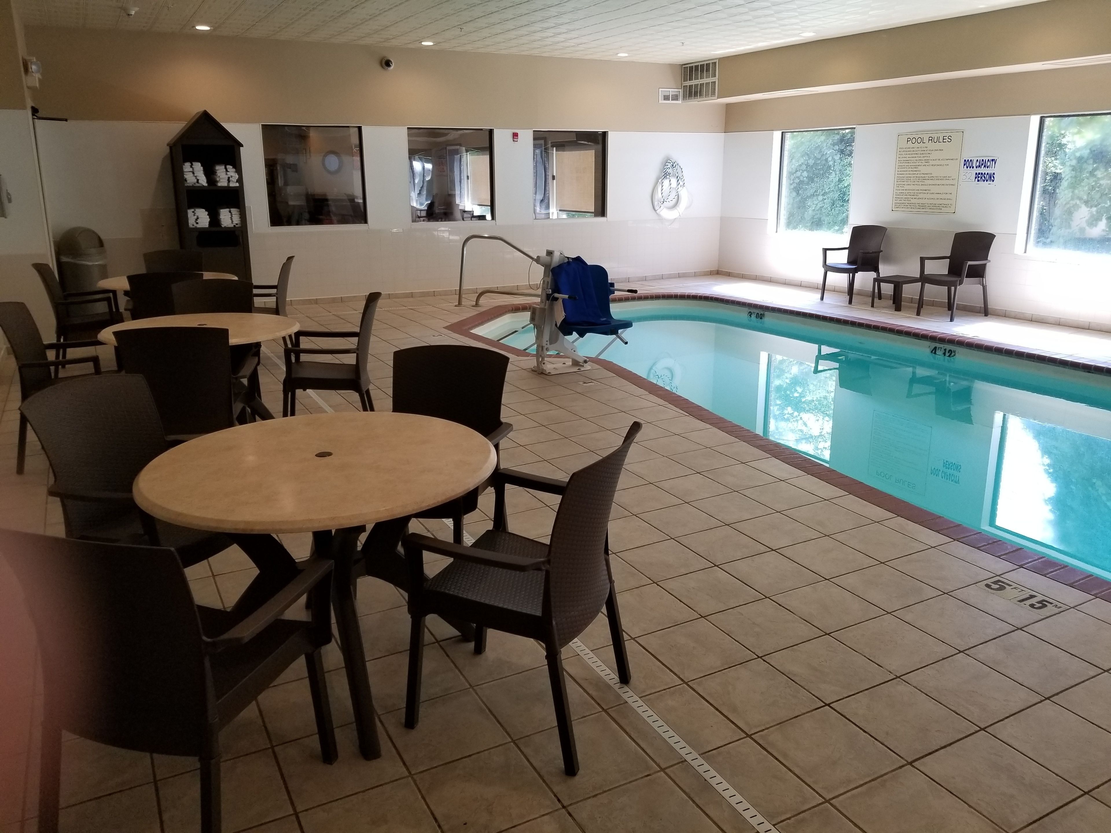 An indoor swimming pool area with tiled flooring, lounge chairs, and a poolside seating area.