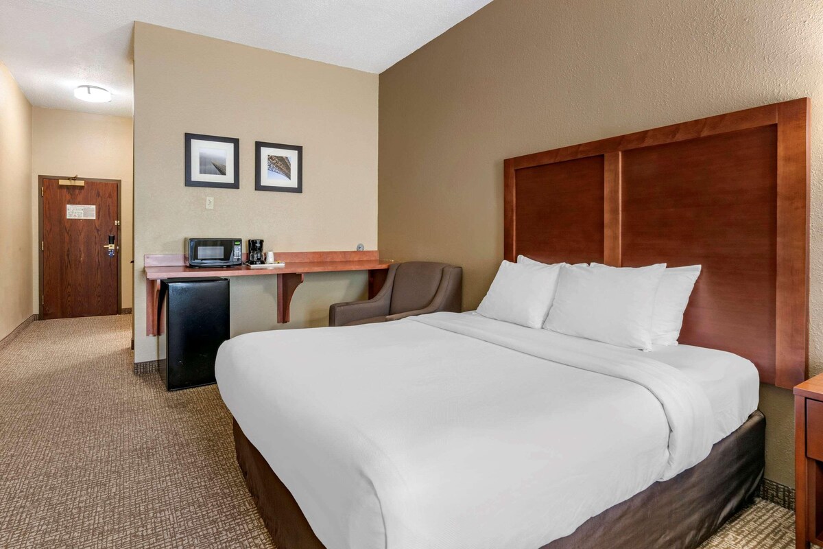 A hotel room with a large bed, a desk with a microwave, a chair, and two framed pictures on the wall.