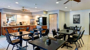A modern kitchen with a microwave, refrigerator, and coffee machine. There are multiple tables and chairs arranged for dining. - SureStay Plus Hotel by Best Western Redding (Redding)