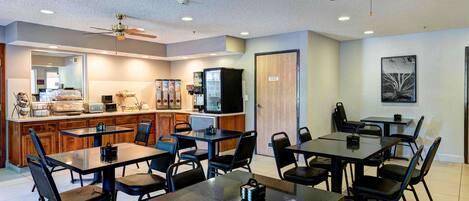 A modern kitchen with a microwave, refrigerator, and coffee machine. There are multiple tables and chairs arranged for dining.