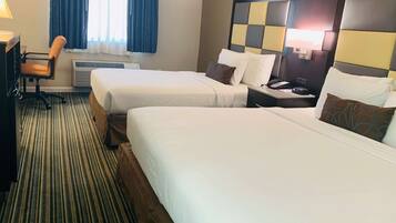 Habitación de hotel con dos camas, un escritorio, una silla y una ventana con cortinas.