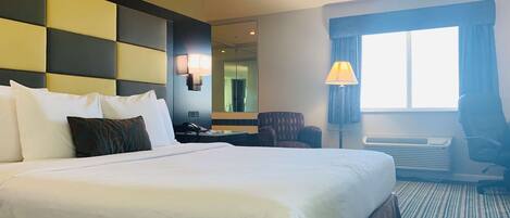A hotel room with a large bed, a desk, a chair, a lamp, and a window with curtains.