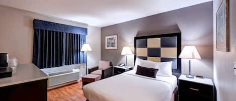 A hotel room with a bed, two bedside tables with lamps, a desk, a chair, a window with curtains, a wall-mounted picture, and a ceiling light.