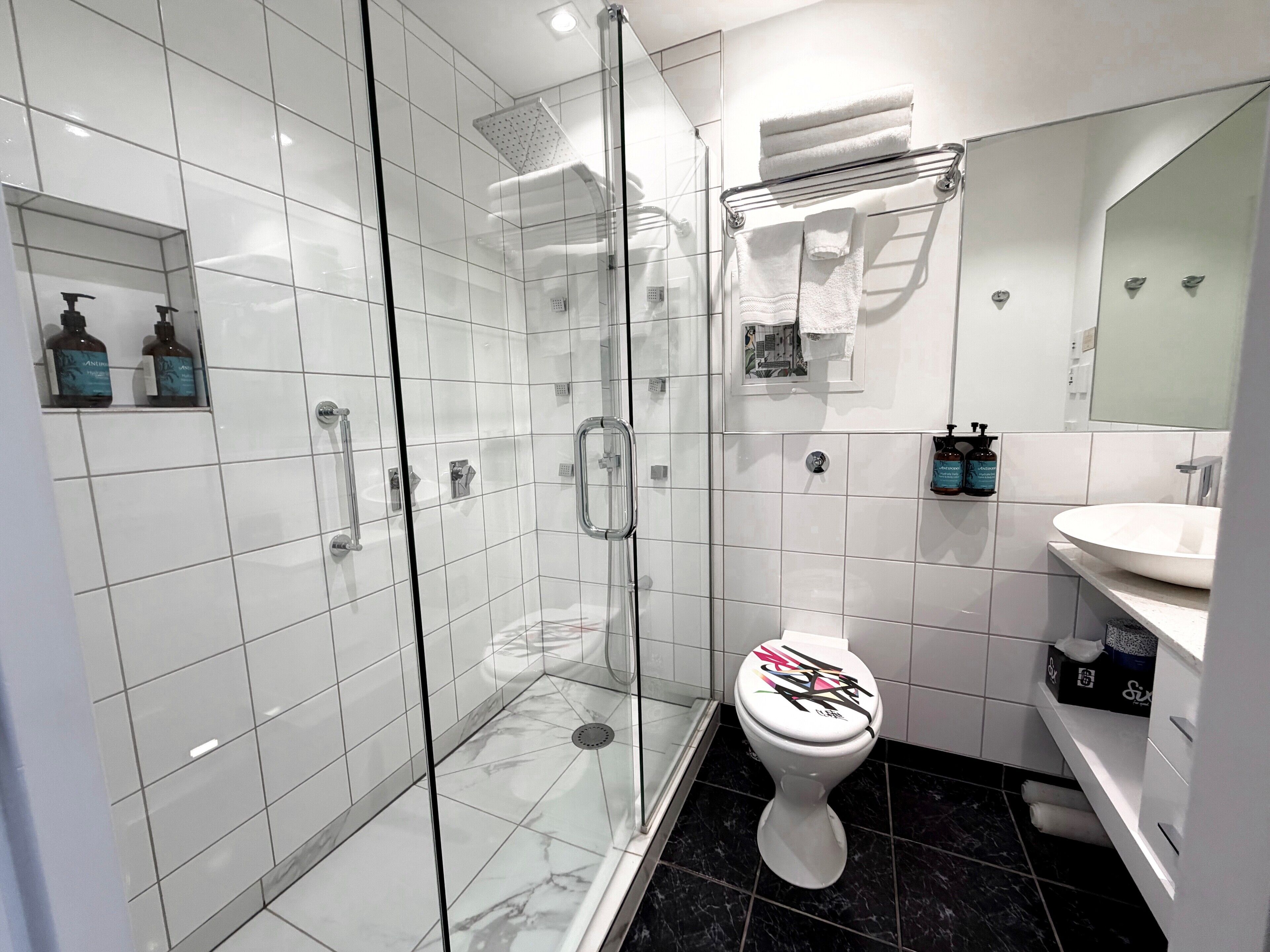 Ein modernes Badezimmer mit einer Duschkabine aus Glas, einer weißen Toilette und einem Waschtisch mit Waschbecken und Spiegel.