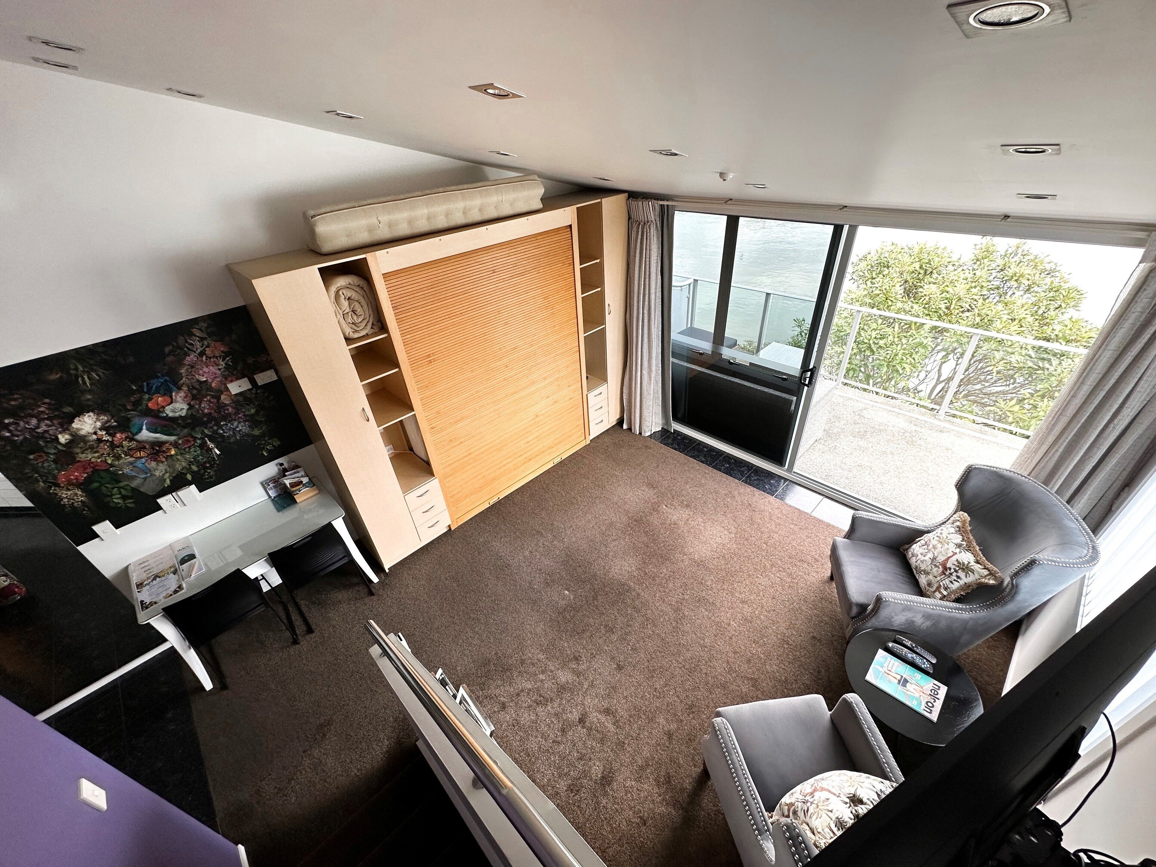 A compact room with a bed, a desk, a chair, and a large window offering a view of the outdoors.
