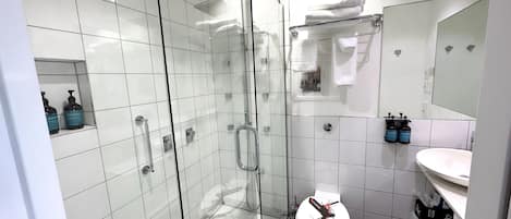 A modern bathroom with a glass-enclosed shower, a toilet with a unique design, and a white sink with a mirror above it.