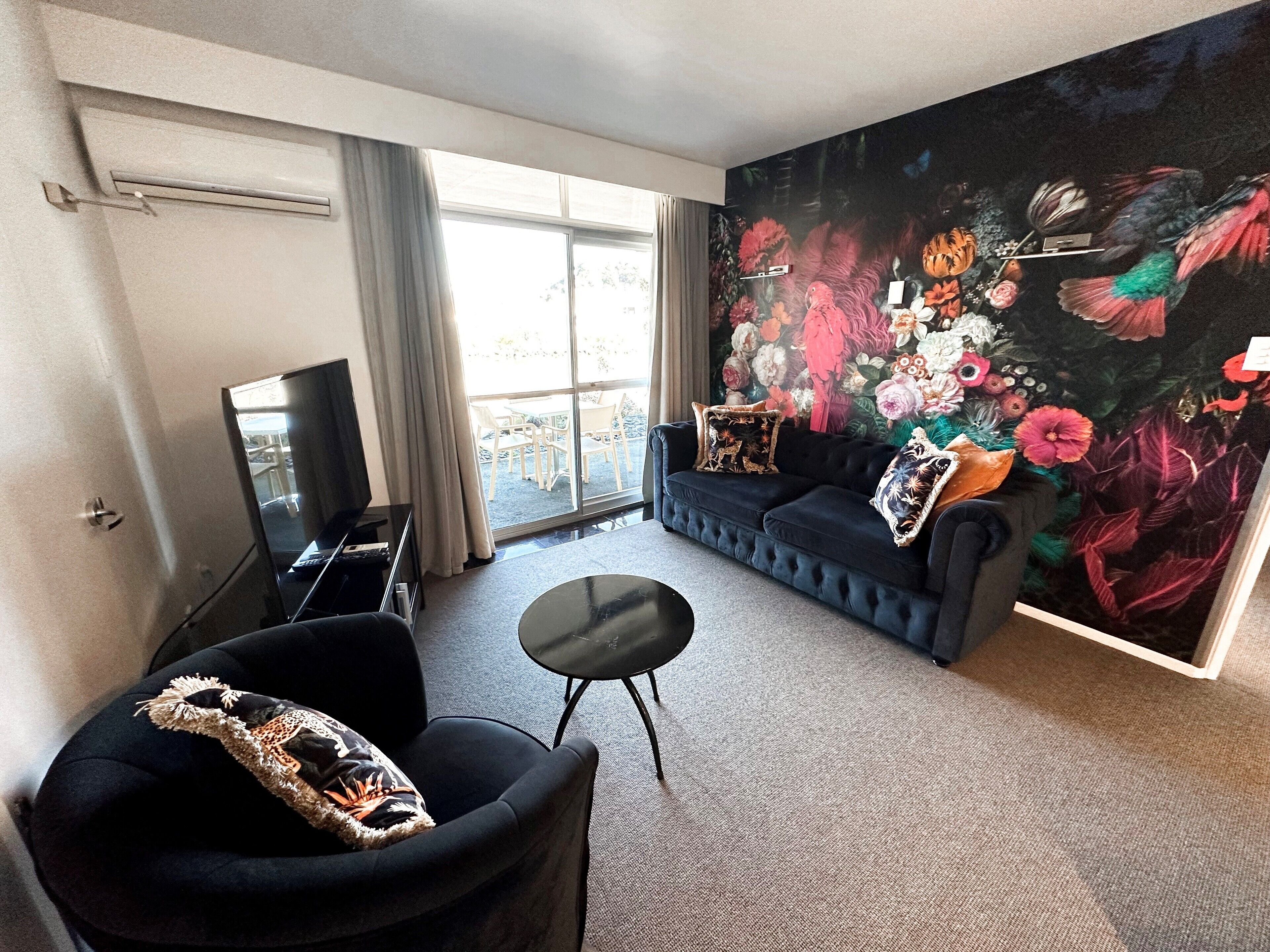 Una sala moderna con un gran mural floral, un sofá oscuro, un sillón negro y una pequeña mesa de centro.