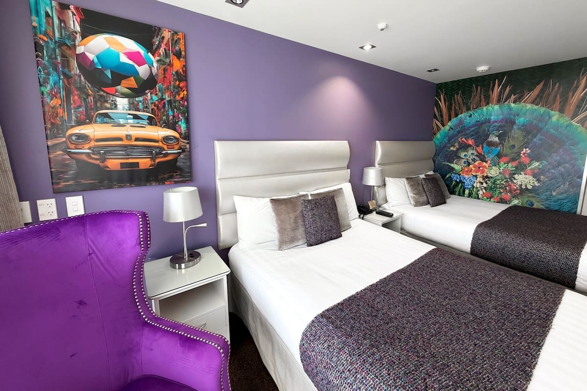 A hotel room with two beds, a purple armchair, and artwork on the walls.
