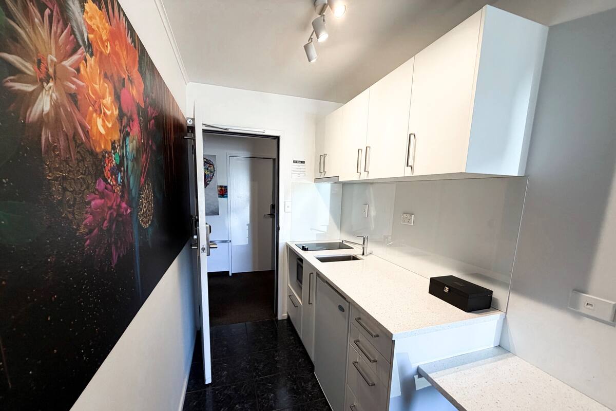 A modern kitchen with white cabinets, a black countertop, and a door leading to another room.