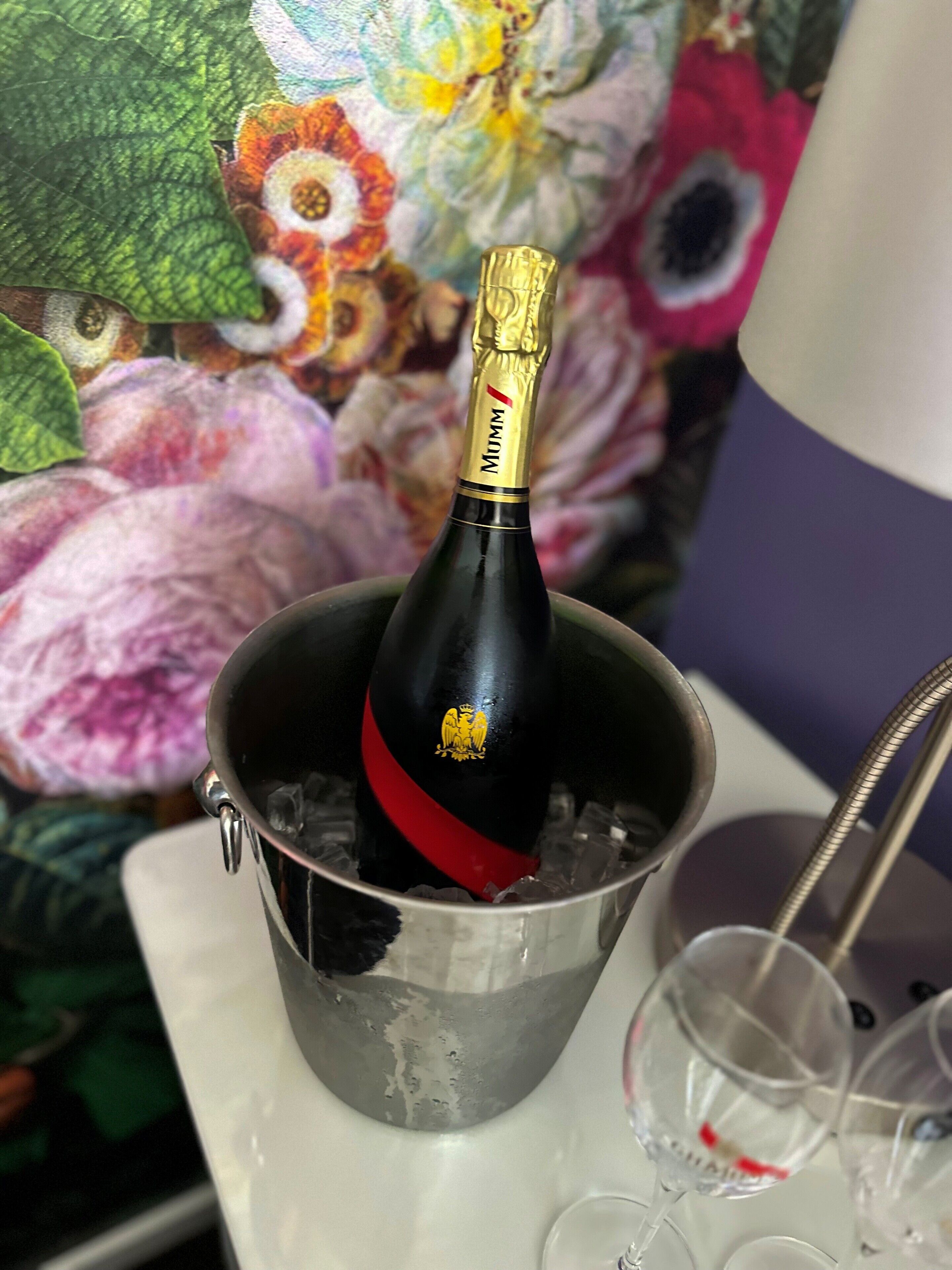 Una botella de champán en un balde metálico con hielo, rodeada de copas y una cuchara.